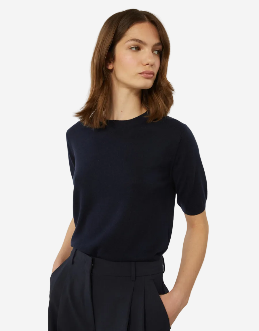 Woman wearing a navy blue top and dark pants on a white background