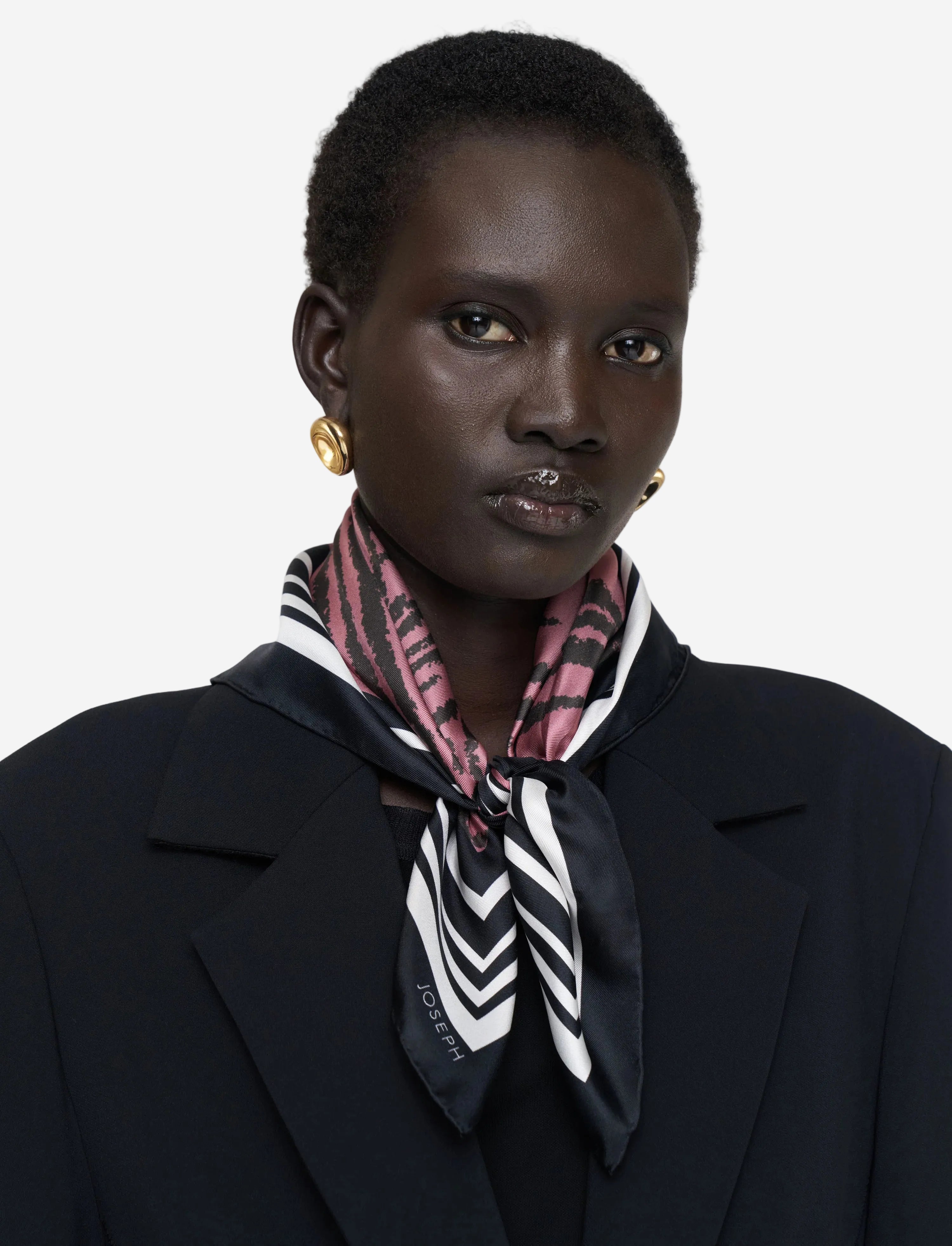 Person wearing a black coat and patterned scarf against a plain background