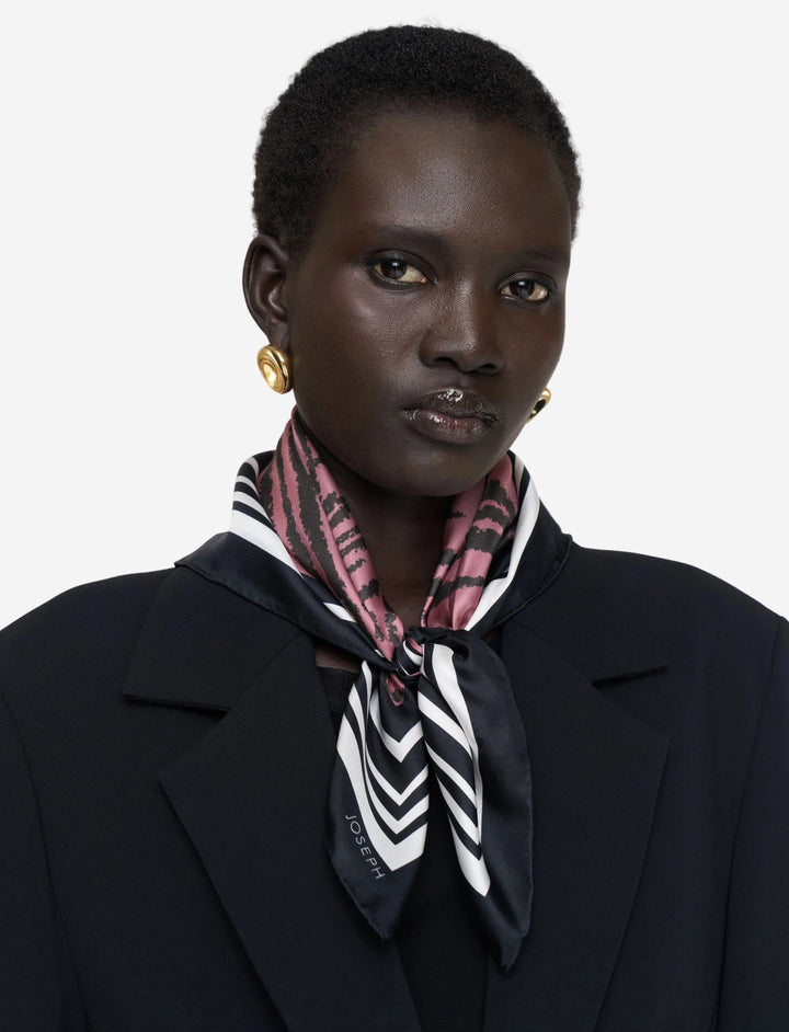 Person wearing a black coat and patterned scarf against a plain background