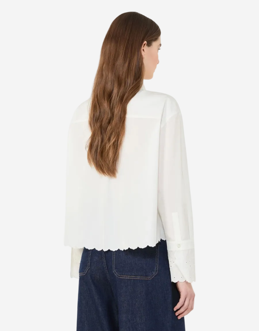 Woman wearing a white blouse with scalloped hem and dark blue jeans on a white background