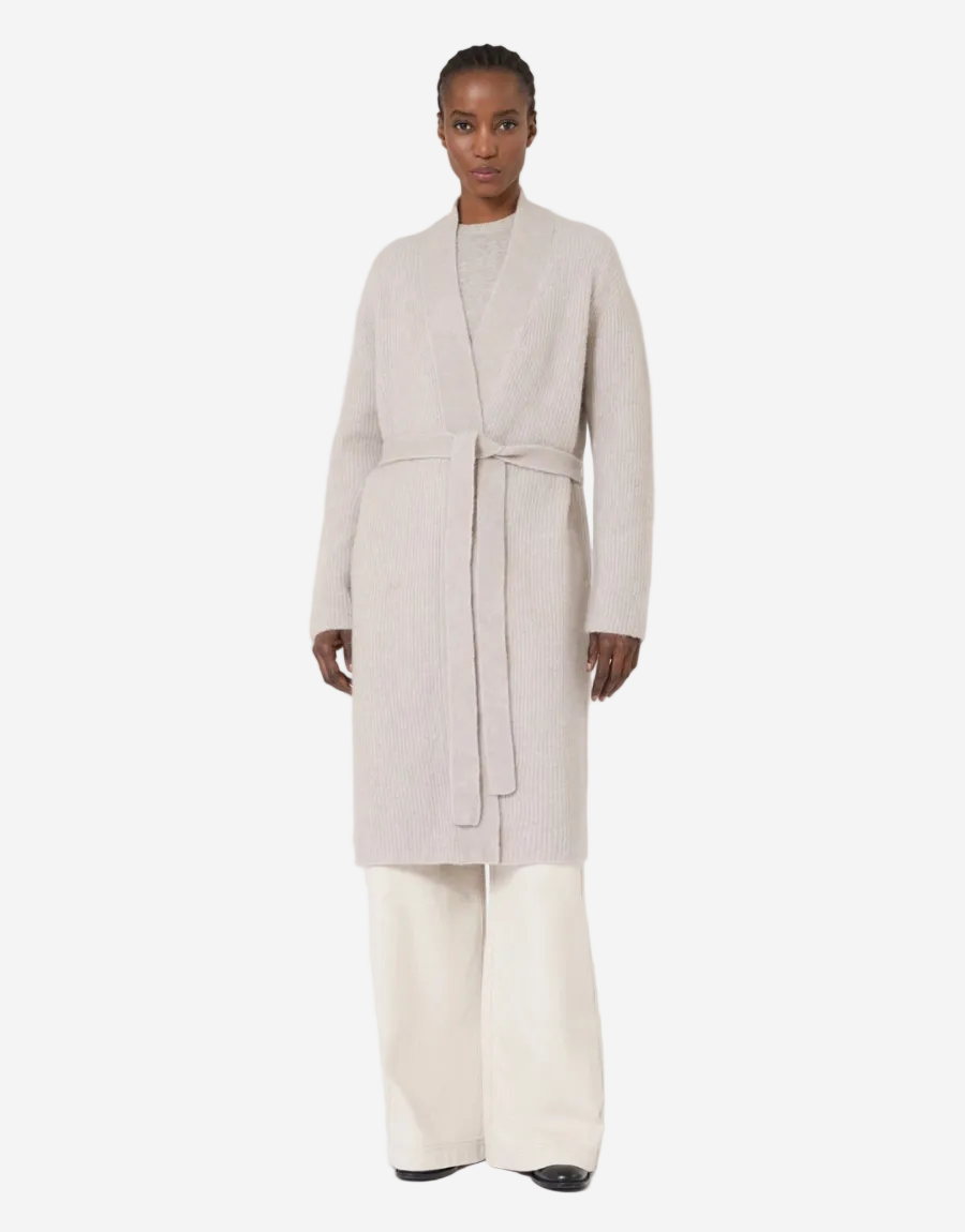 Woman wearing a long beige coat and white pants on a white background