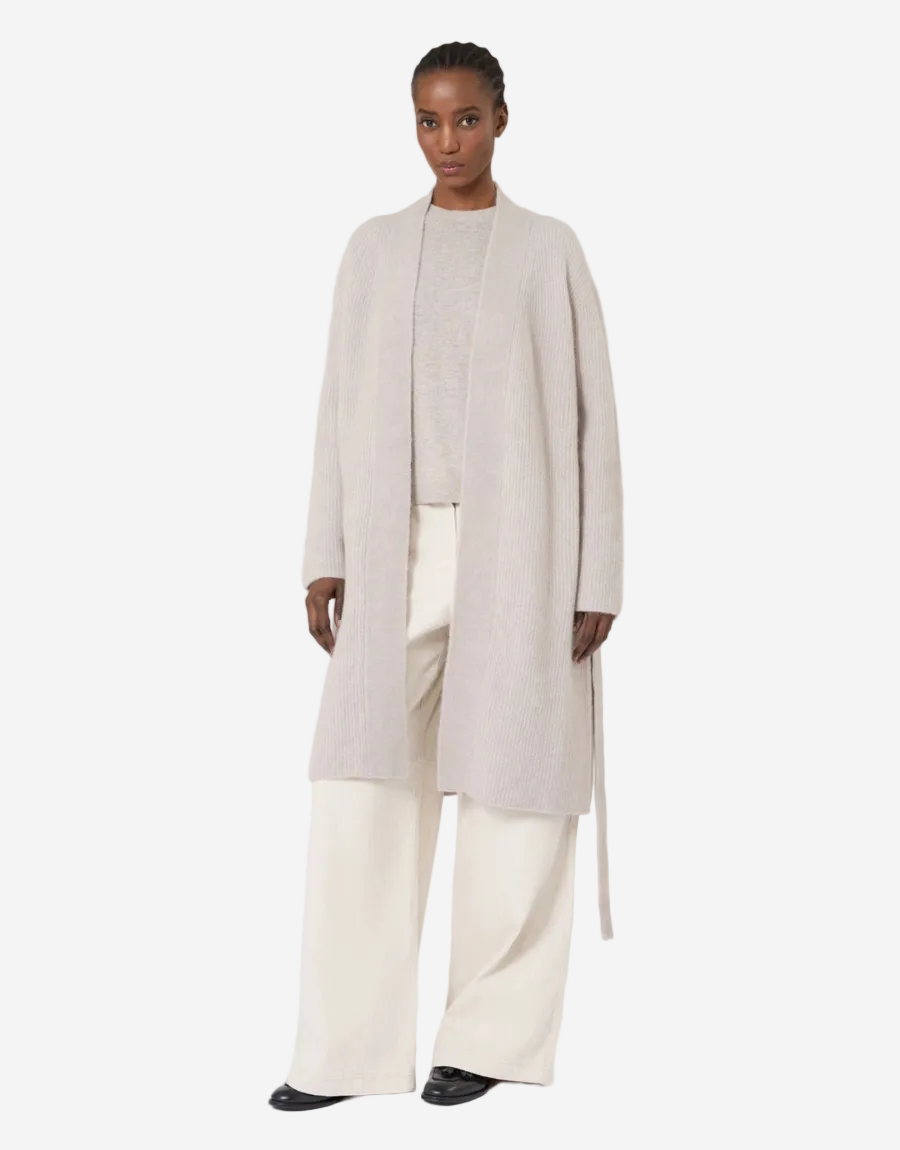 Woman wearing a long beige coat over a white outfit on a white background