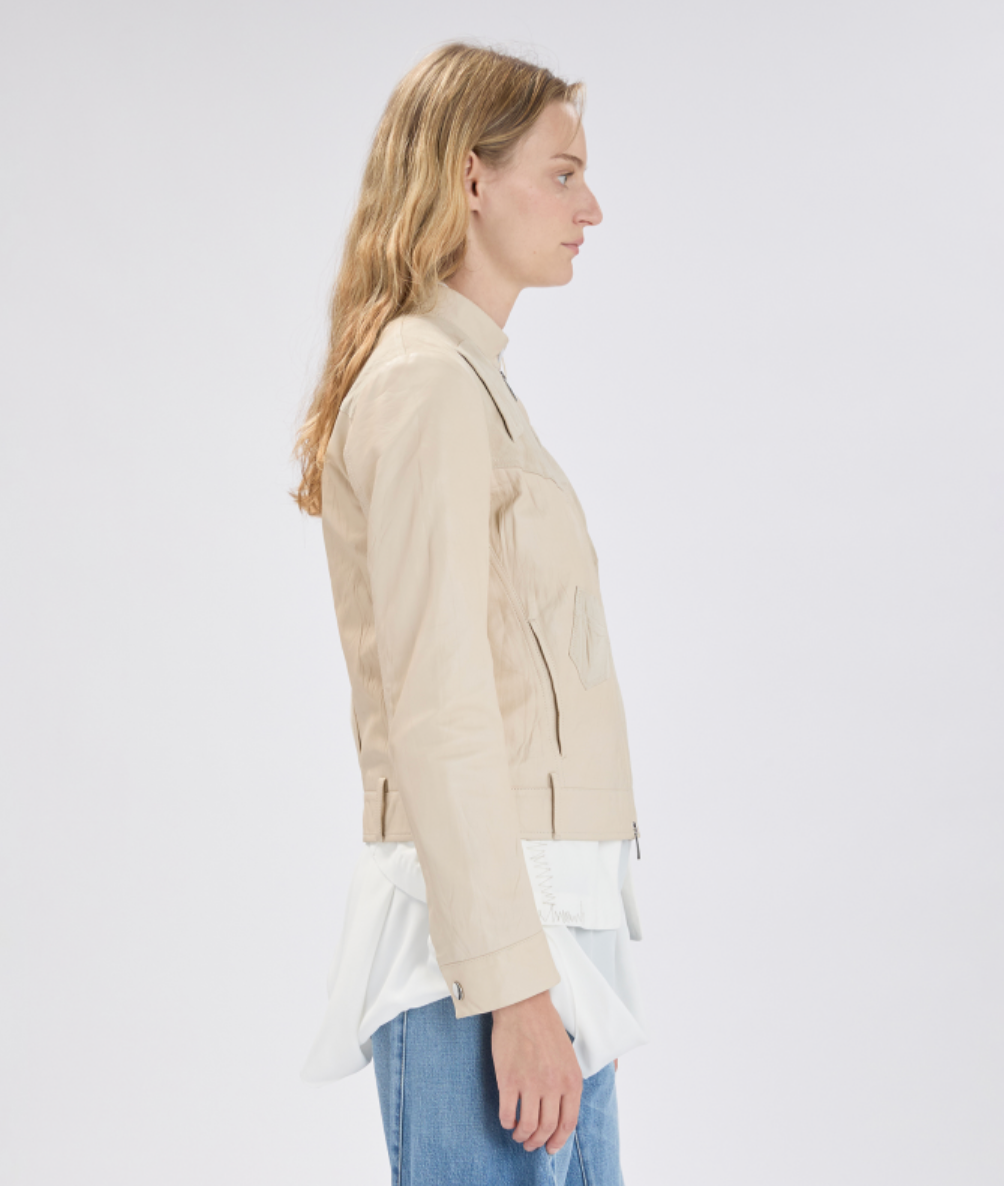 Woman wearing a beige blazer over a white shirt with blue jeans on a light gray background