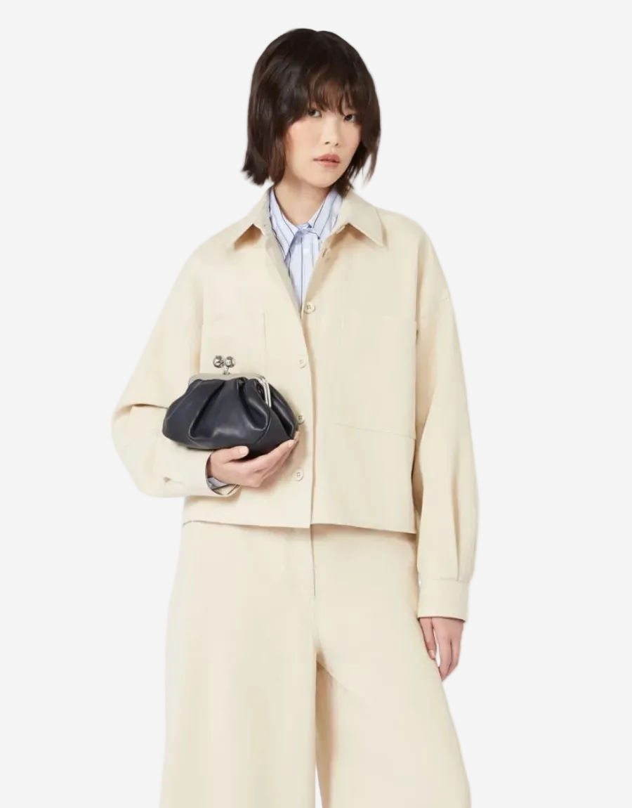 Person wearing a beige outfit holding a black clutch against a white background