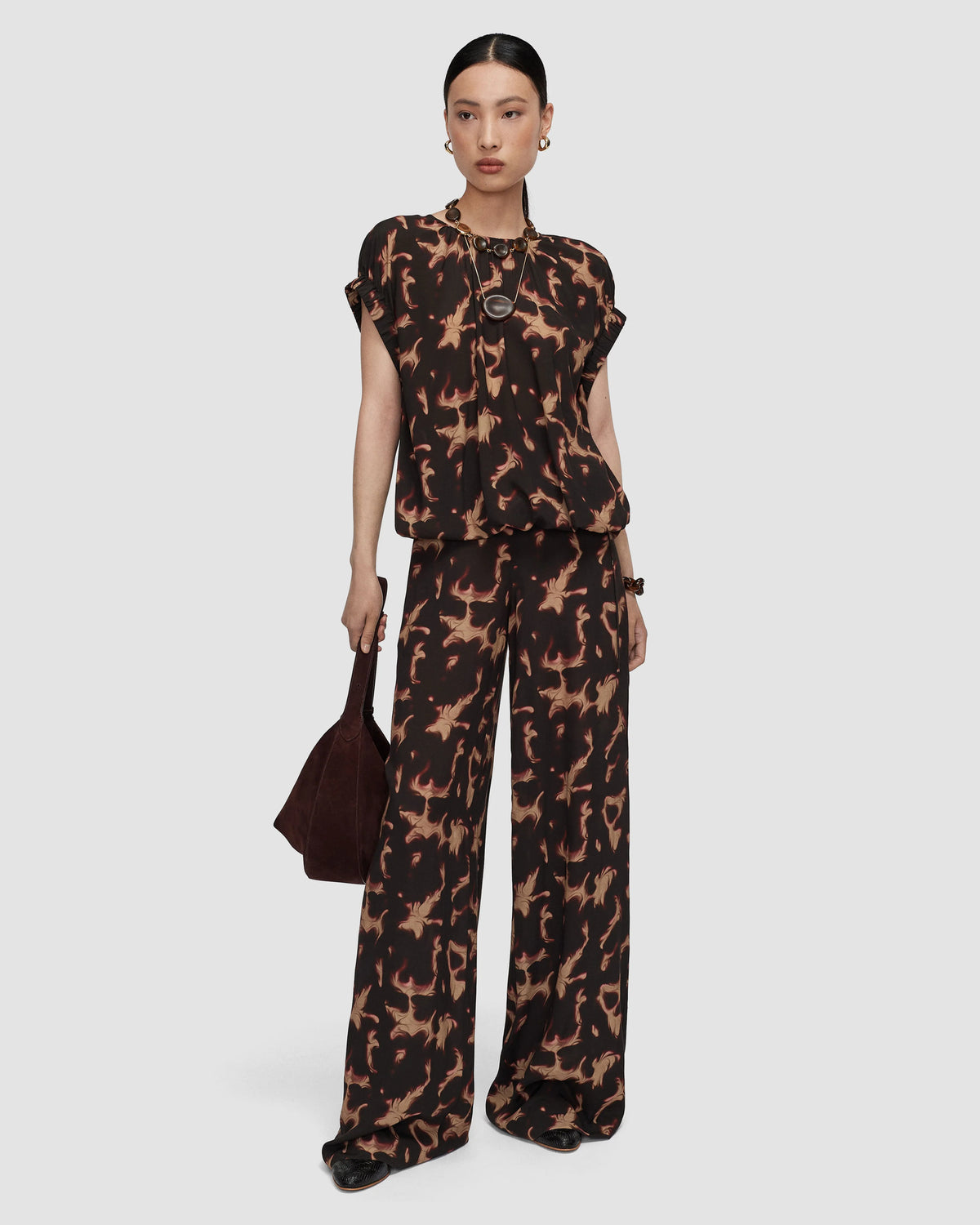 Model wearing a short sleeved dark brown and tan organic abstract patterned top by Joseph.  