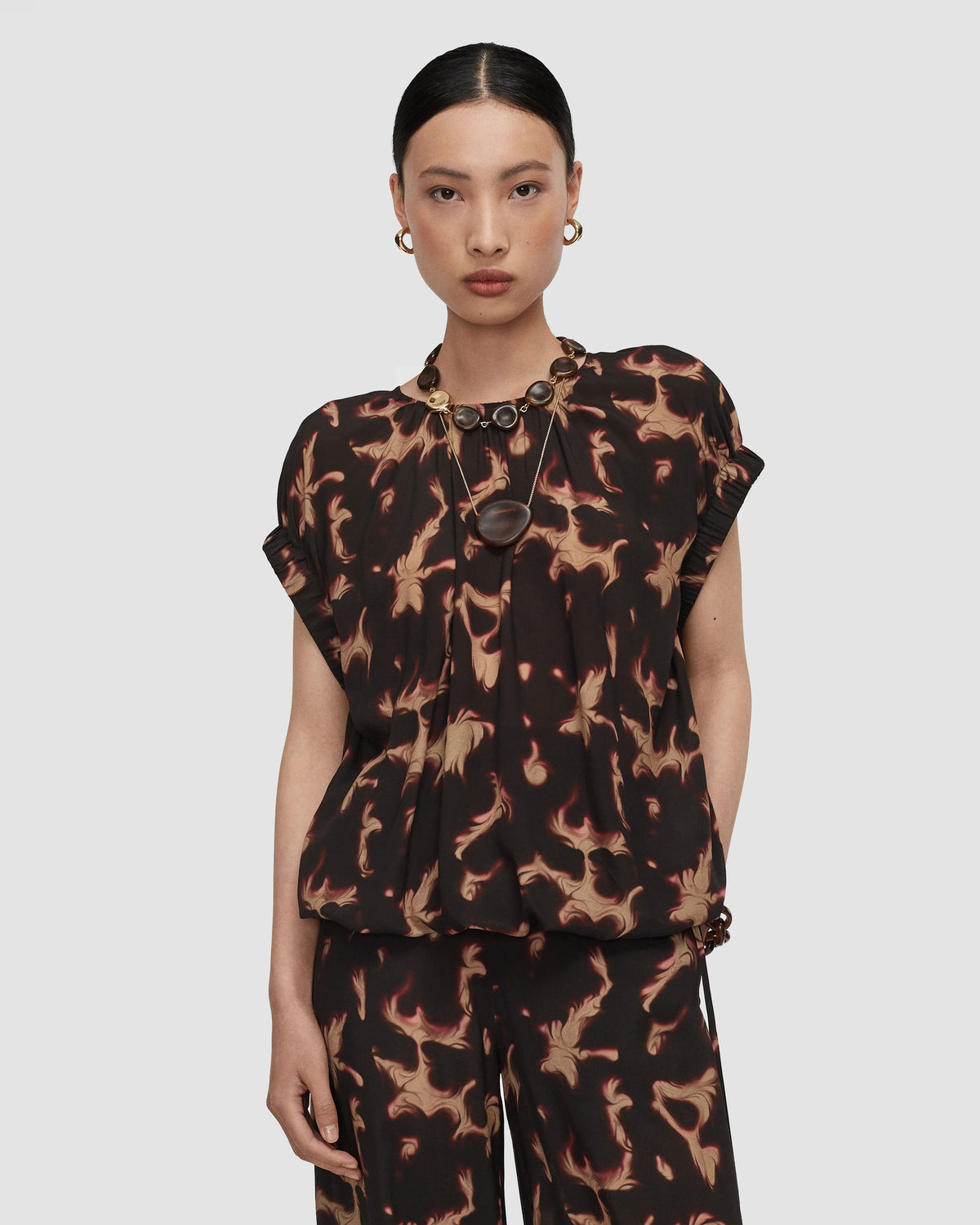 Model wearing a short sleeved dark brown and tan organic abstract patterned top from Christensen Copenhagen.  