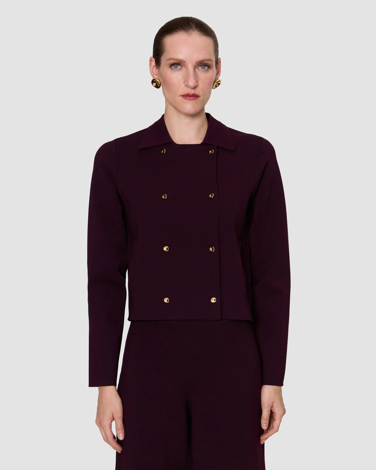 model wearing a deep burgundy double-breasted coat with gold buttons and a structured collar from Christensen Copenhagen. 