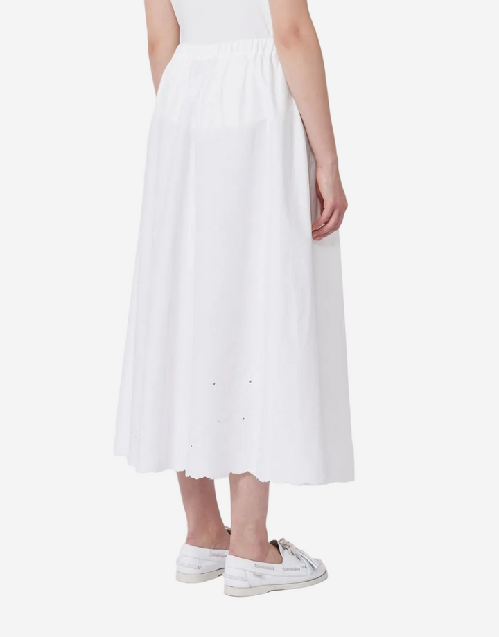 Person wearing a white skirt and white sneakers on a plain background