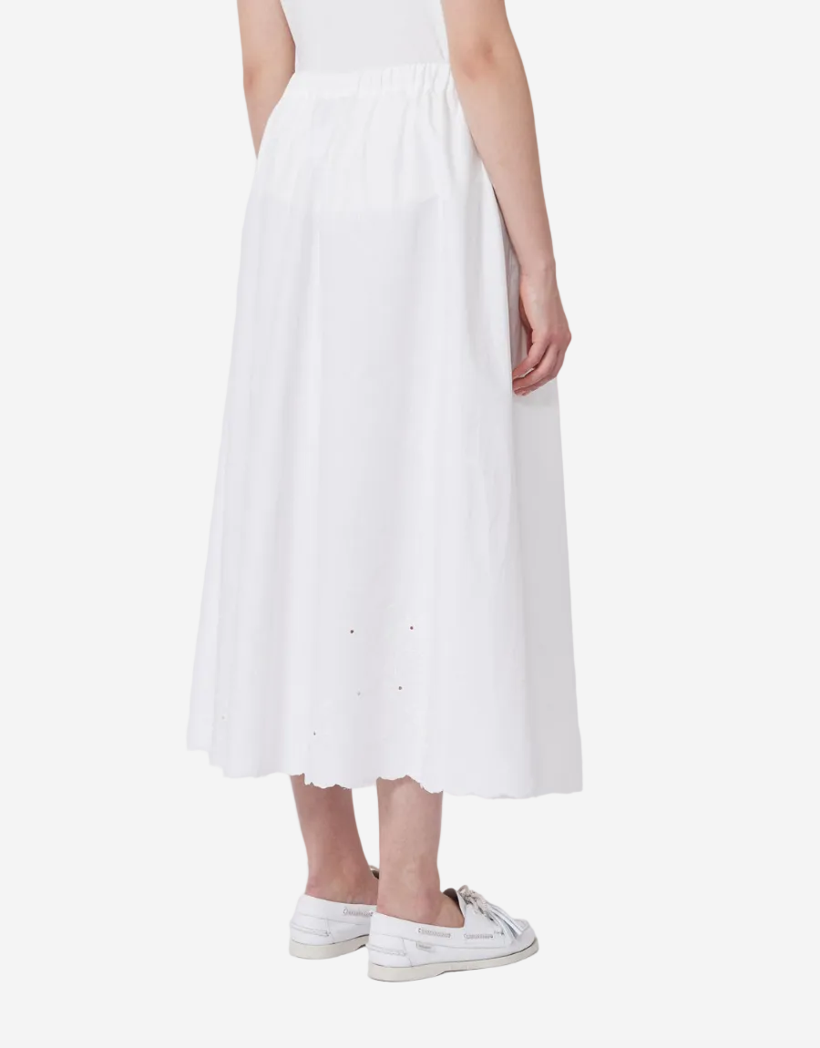 Person wearing a white skirt and white sneakers on a plain background