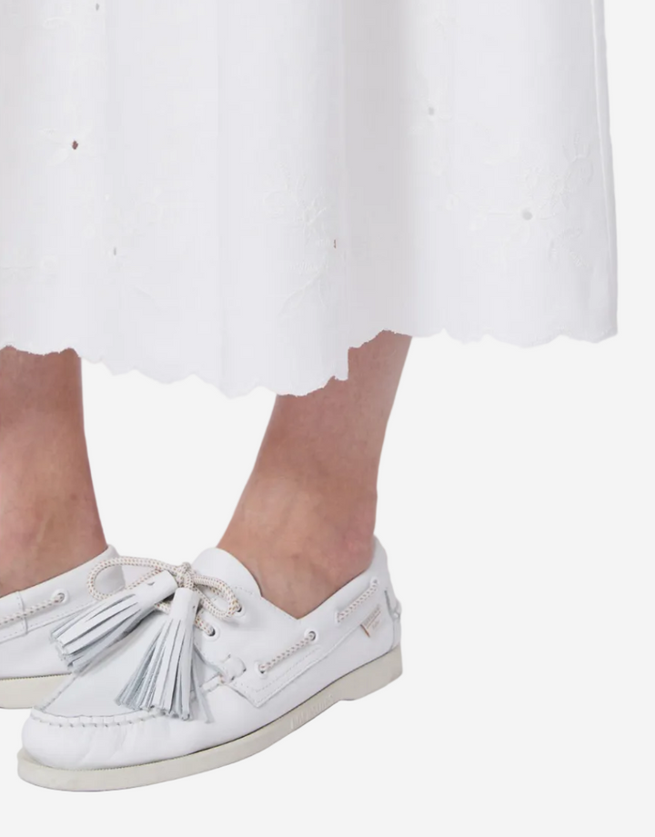 White skirt with scalloped hem worn by a person on a white background
