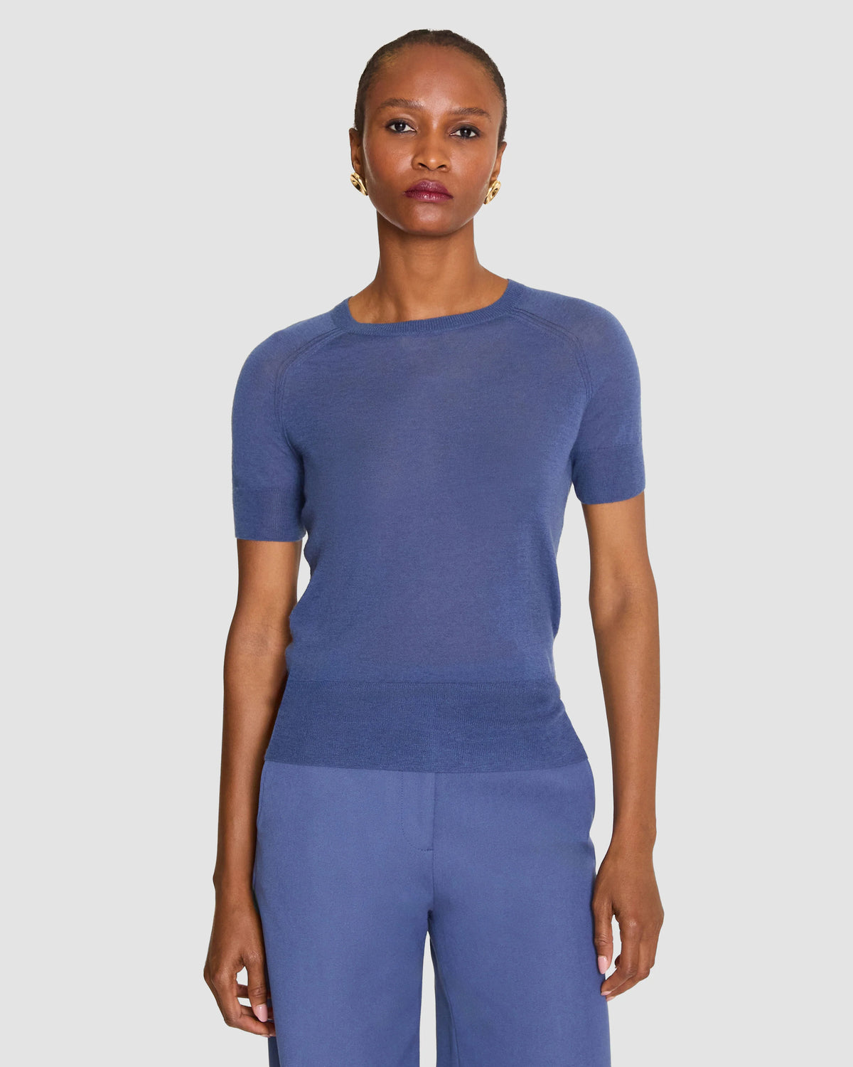 A model wearing a short-sleeve crewneck knit top in a dusty periwinkle blue by Joseph. 