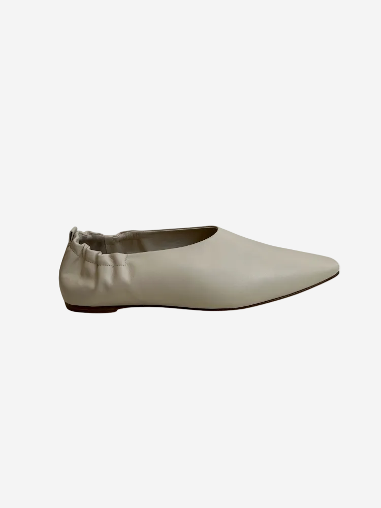 A beige leather loafer with a pointed toe and minimalistic design, featuring a small buckle strap.