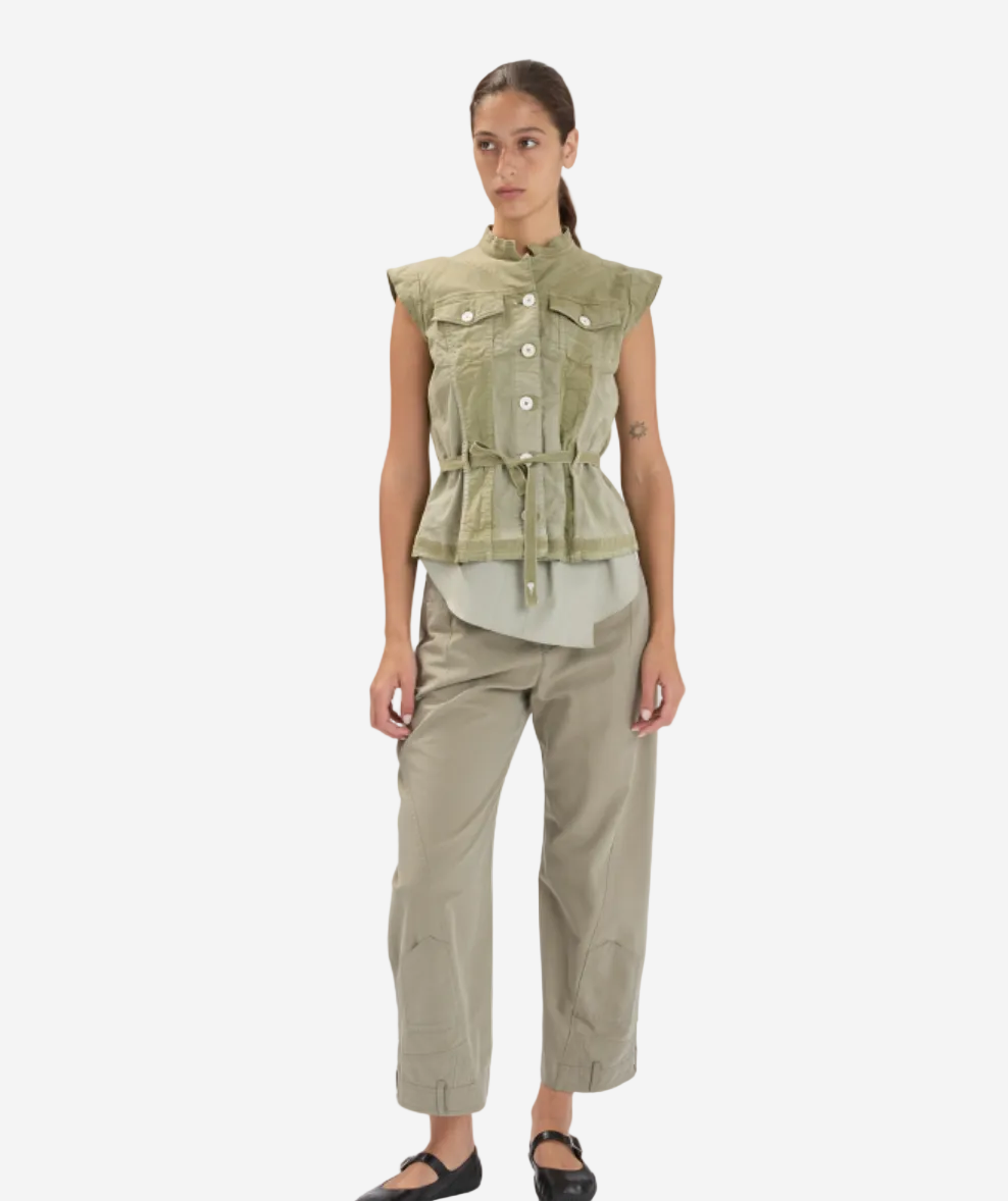 Woman wearing a sleeveless green jacket and beige pants on a white background