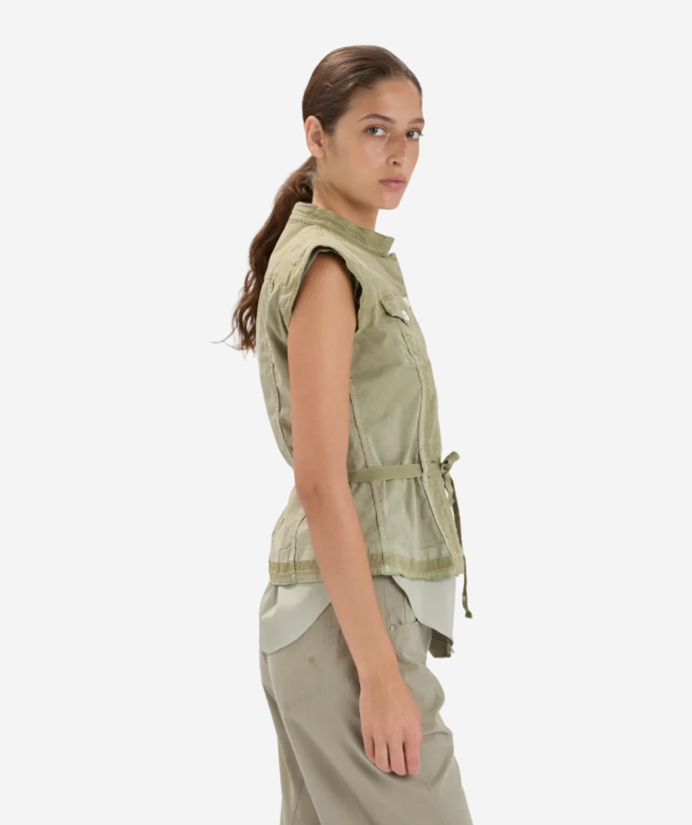 Woman wearing a sleeveless green jacket and beige pants on a white background