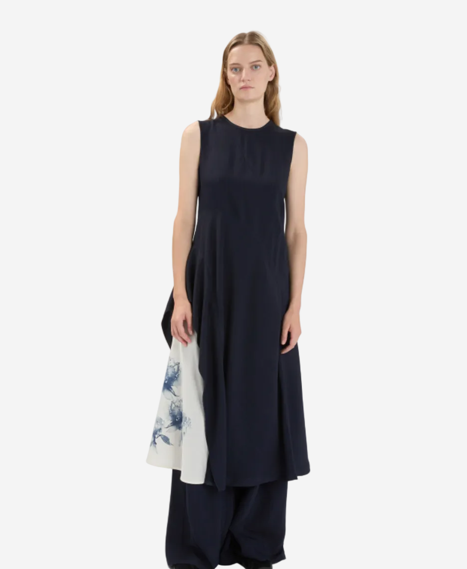 Woman wearing a black sleeveless dress holding a white bag with floral design on a white background