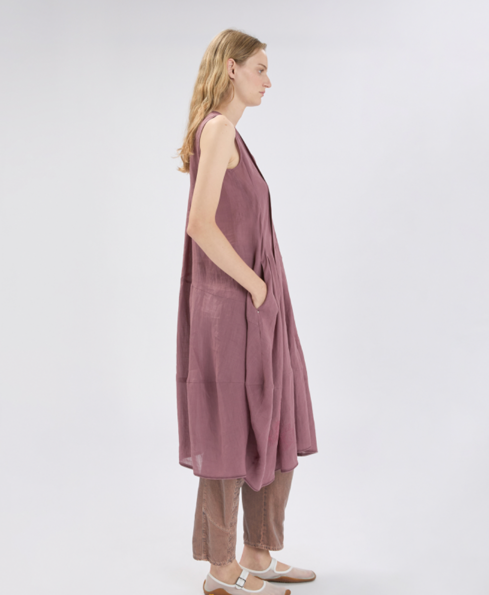Woman wearing a sleeveless, mauve dress with a plain background
