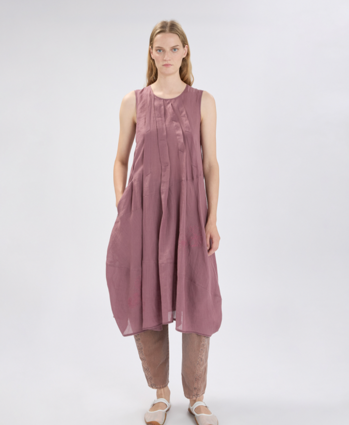 Woman wearing a sleeveless, long, mauve dress on a white background