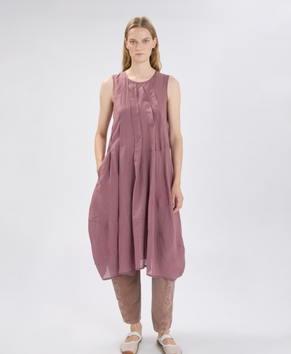 Woman wearing a sleeveless, long, mauve dress on a white background