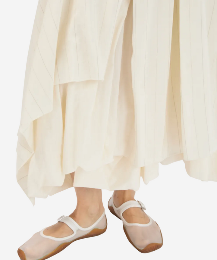 Person wearing white ballet flats and a flowing white dress on a light background