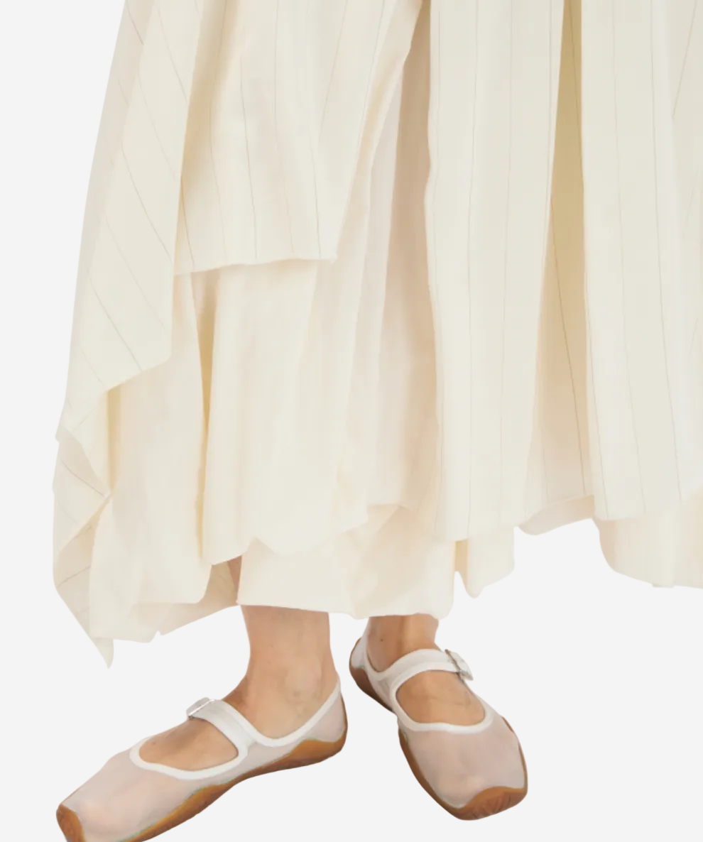 Person wearing white ballet flats and a flowing white dress on a light background
