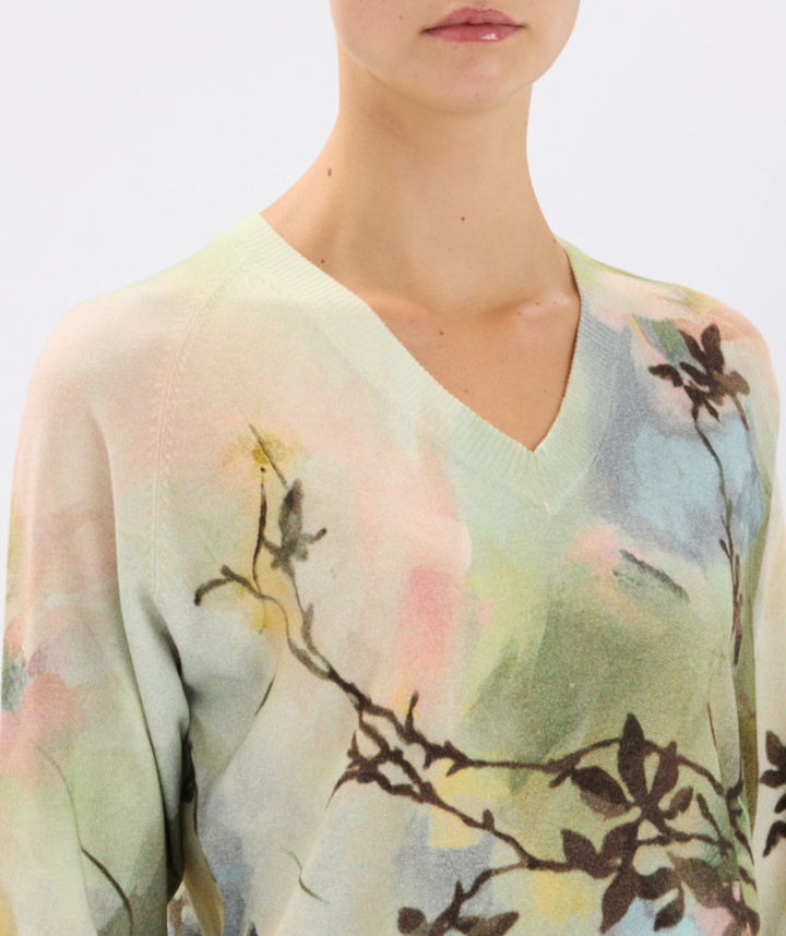 Light green sweater with floral pattern worn by a person on a white background