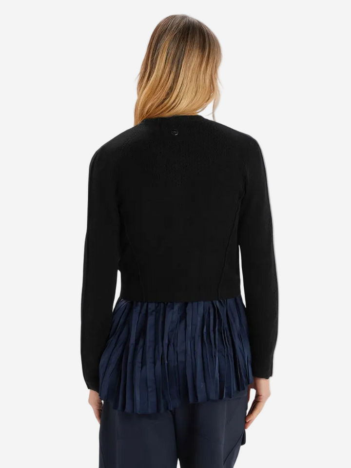 Person wearing a black sweater with a navy pleated skirt on a white background