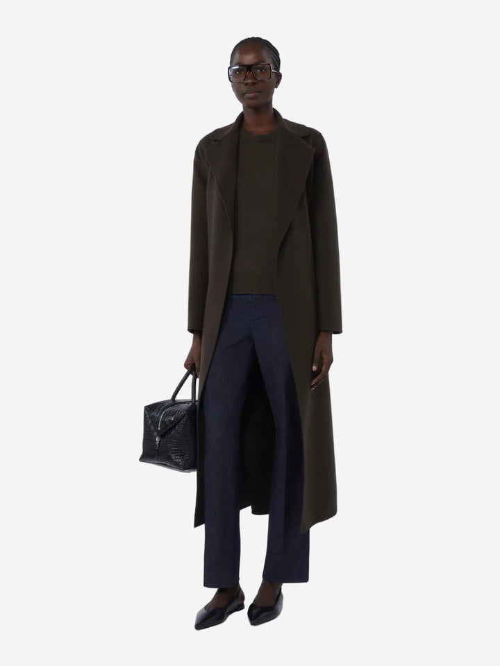 Person wearing a long dark coat and holding a black bag on a white background