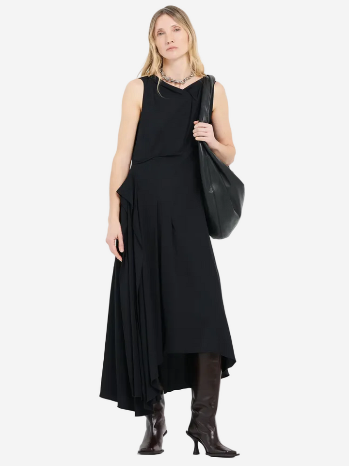 Woman wearing a black sleeveless dress and boots, holding a black bag on a white background