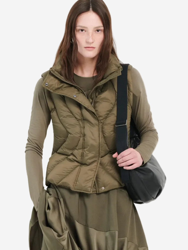 Woman wearing a green quilted jacket and holding a black bag on a white background