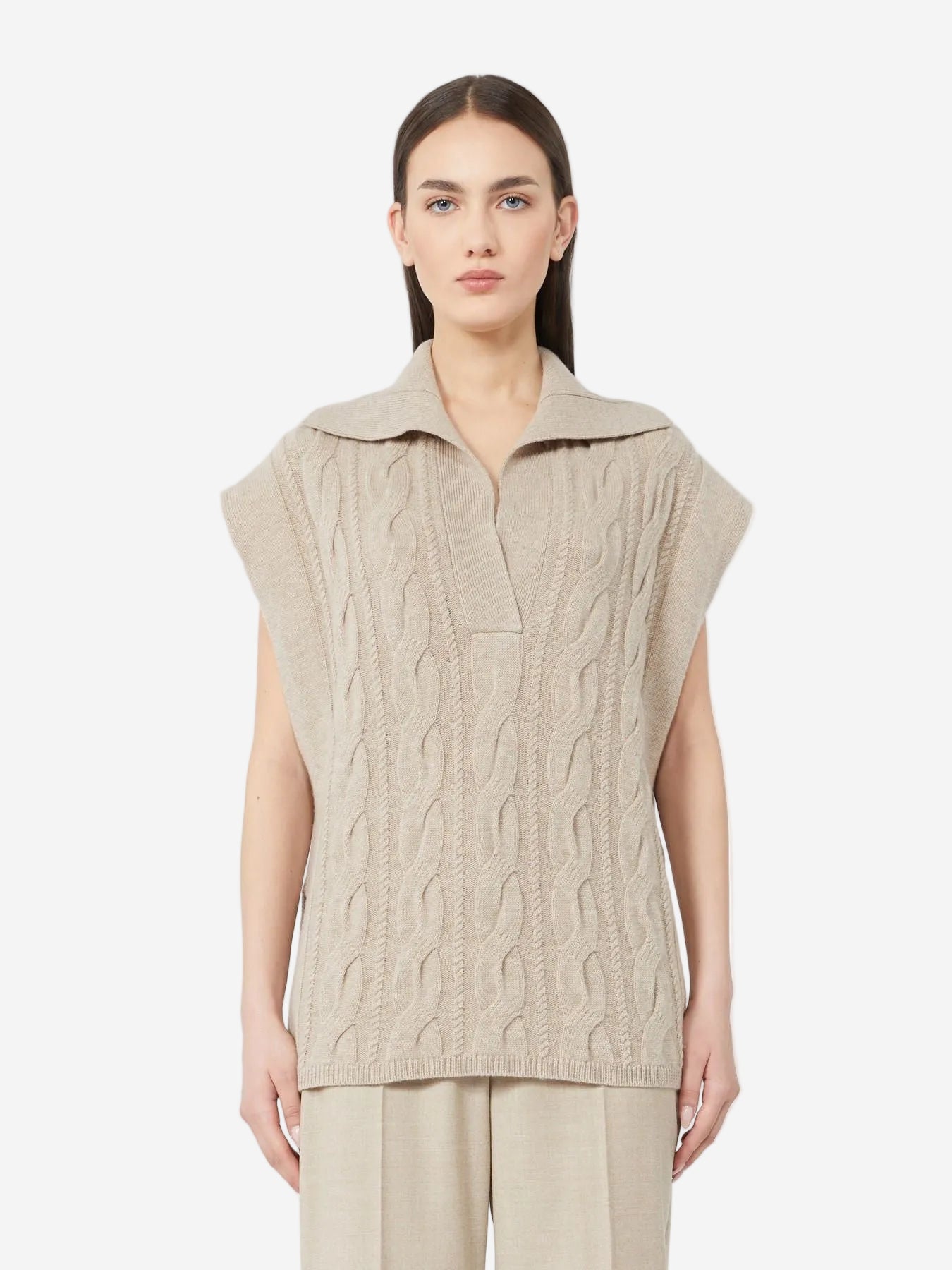 Woman wearing a beige cable knit sleeveless sweater on a white background