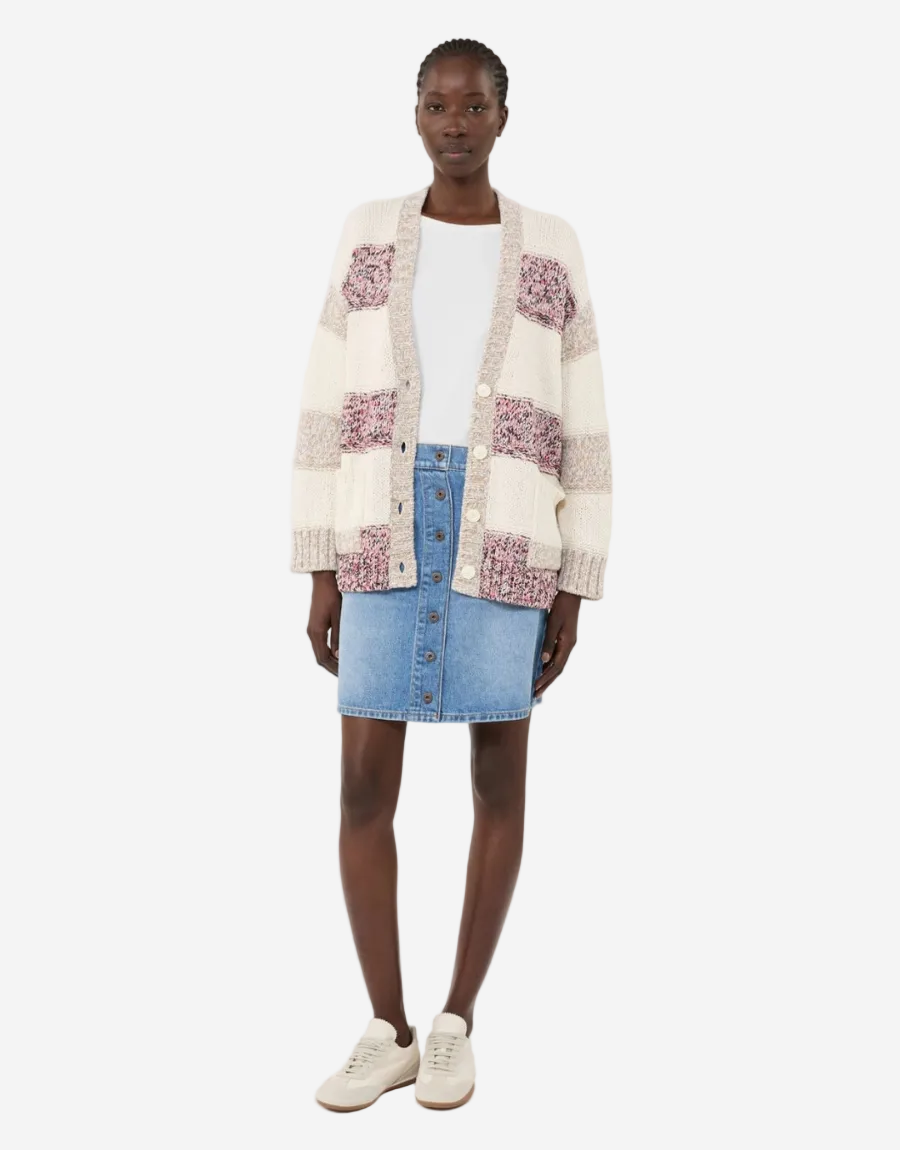 Person wearing a patterned cardigan, white top, blue denim skirt, and white sneakers on a white background