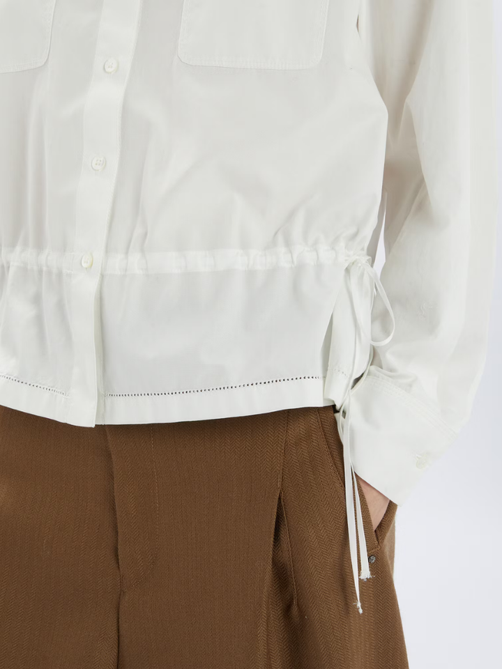 White shirt with drawstring details worn with brown pants on a white background