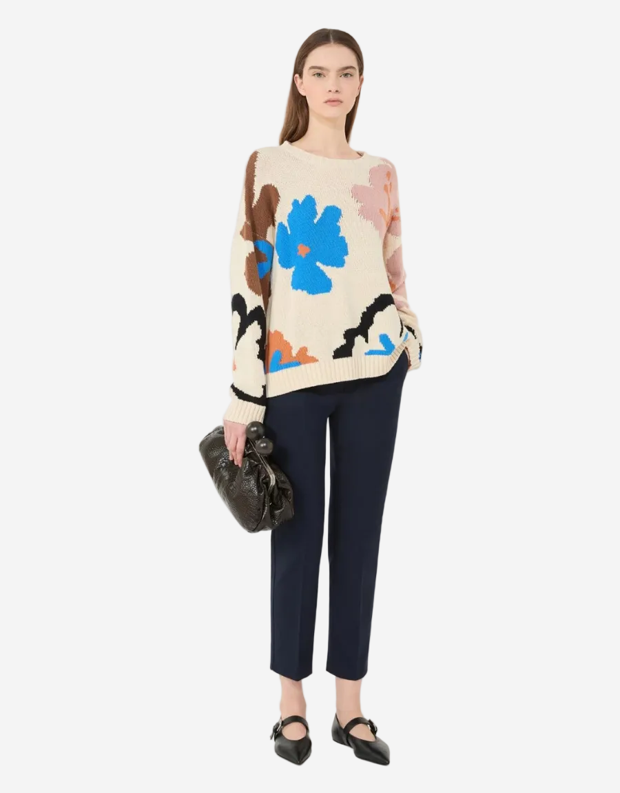 Woman wearing a colorful floral sweater and dark pants on a white background