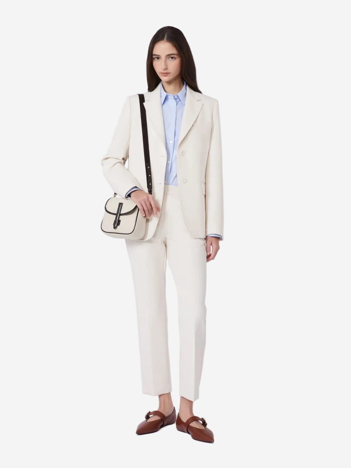 Woman wearing a cream suit with a blue shirt, carrying a black and white handbag on a white background