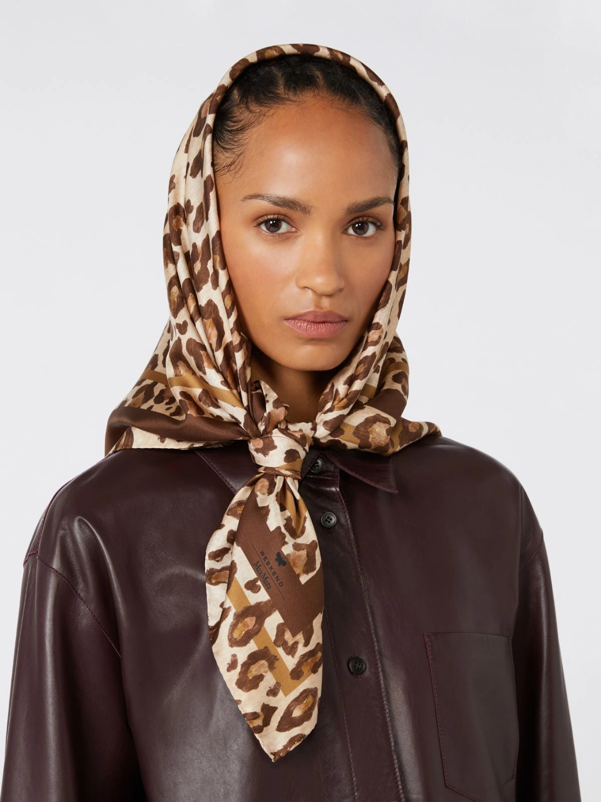 Woman wearing a leopard print headscarf and brown leather jacket on a white background