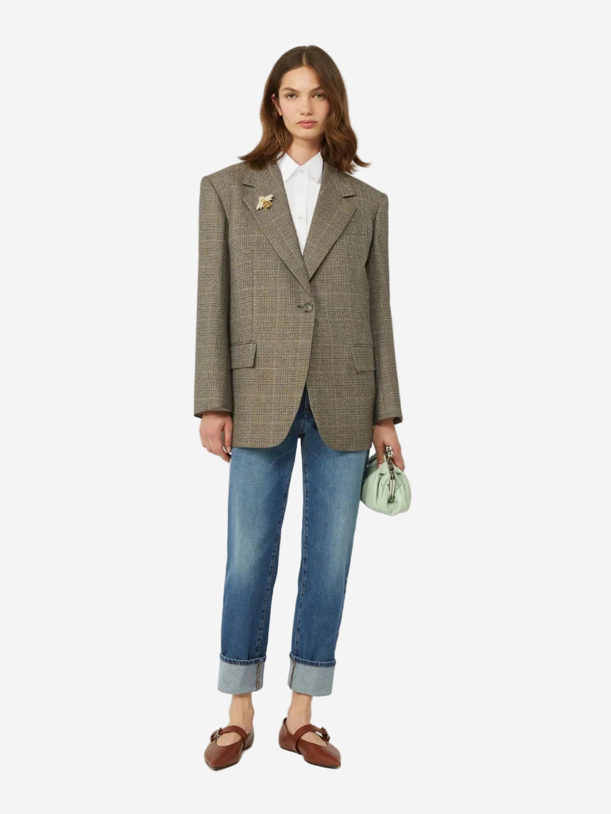 Woman wearing a brown checkered blazer, white shirt, blue jeans, and brown shoes on a white background.