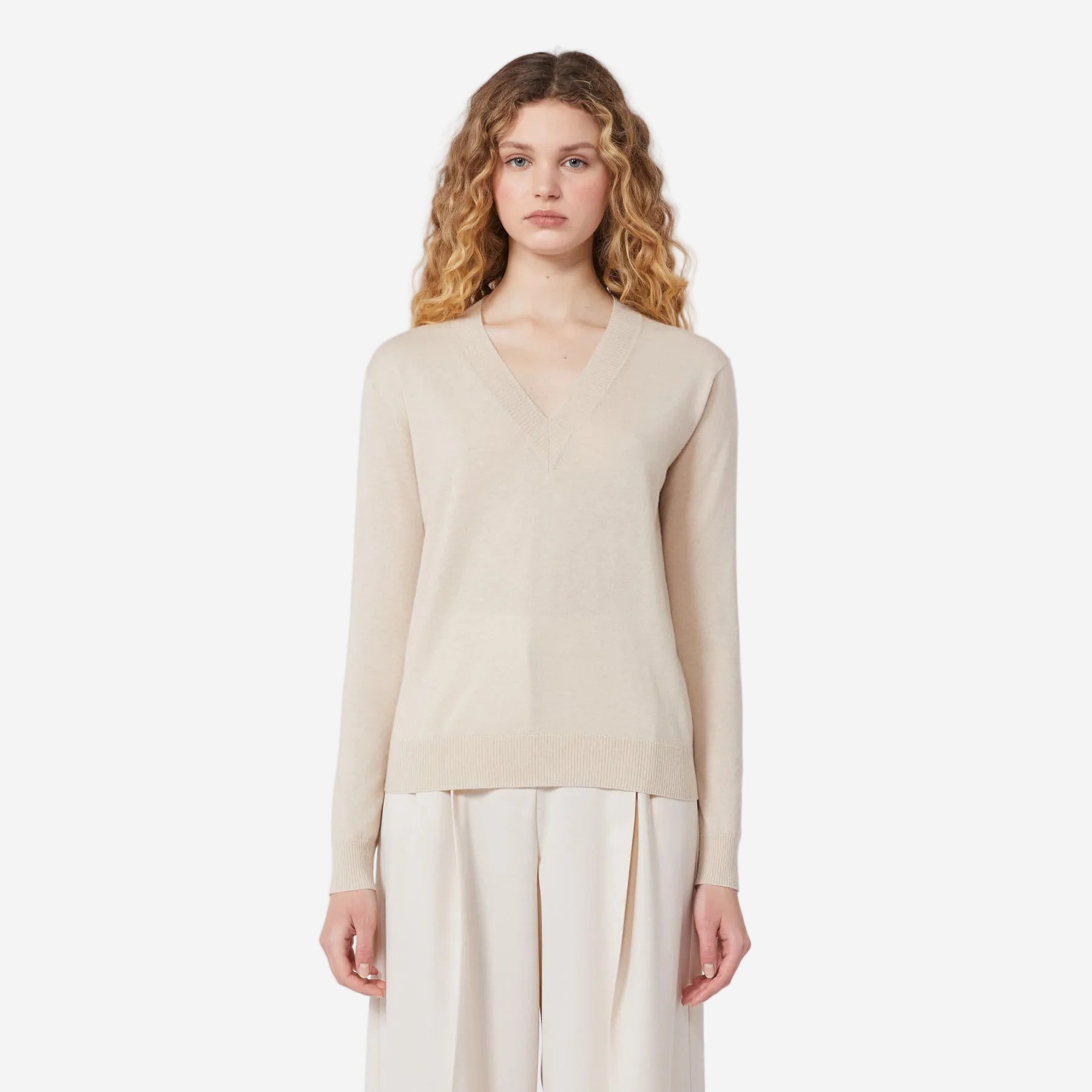 Woman wearing a beige long-sleeve top and white pants on a white background