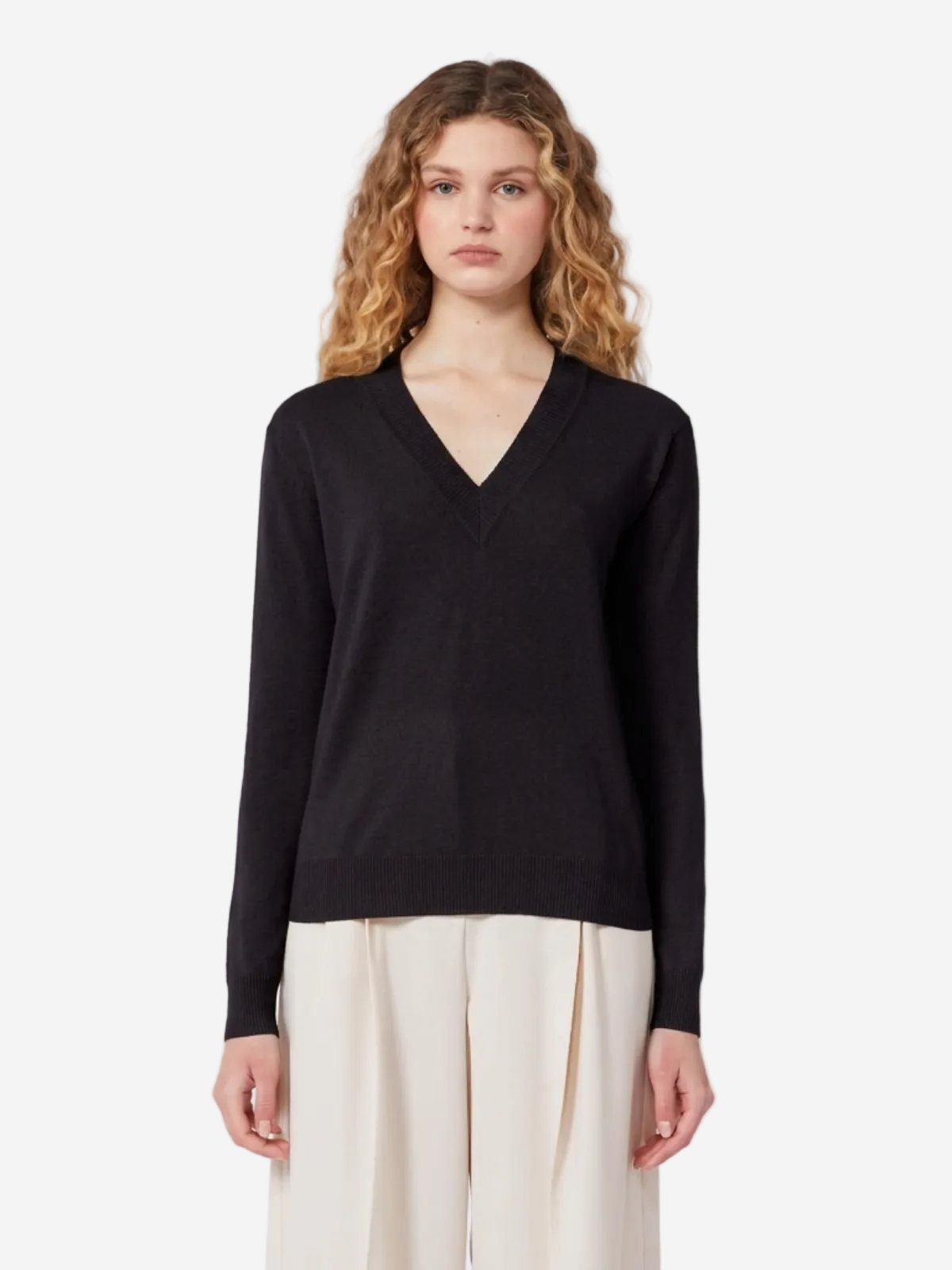 Woman wearing a black V-neck sweater and white pants on a light gray background