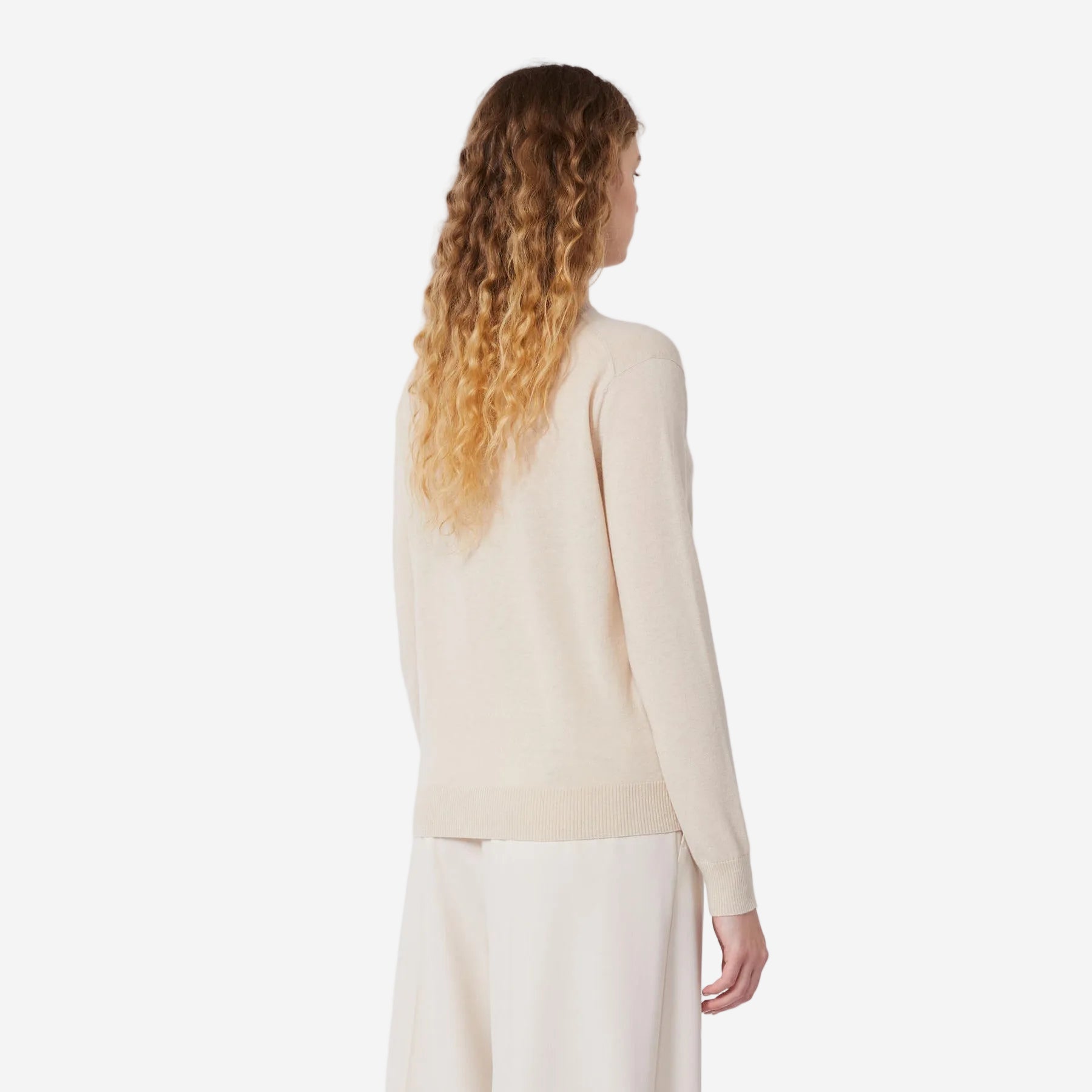 Woman wearing a beige long-sleeve top and white pants on a white background