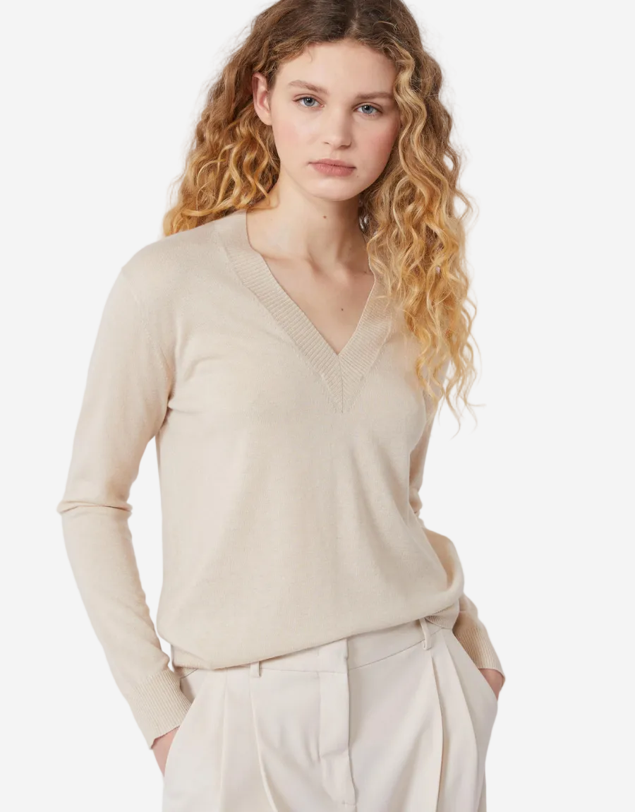 Woman wearing a beige sweater and white pants on a white background