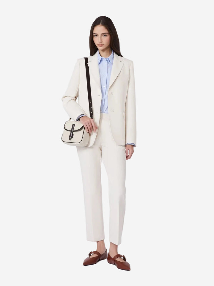 Woman wearing a cream suit with a blue shirt, carrying a black and white handbag on a white background