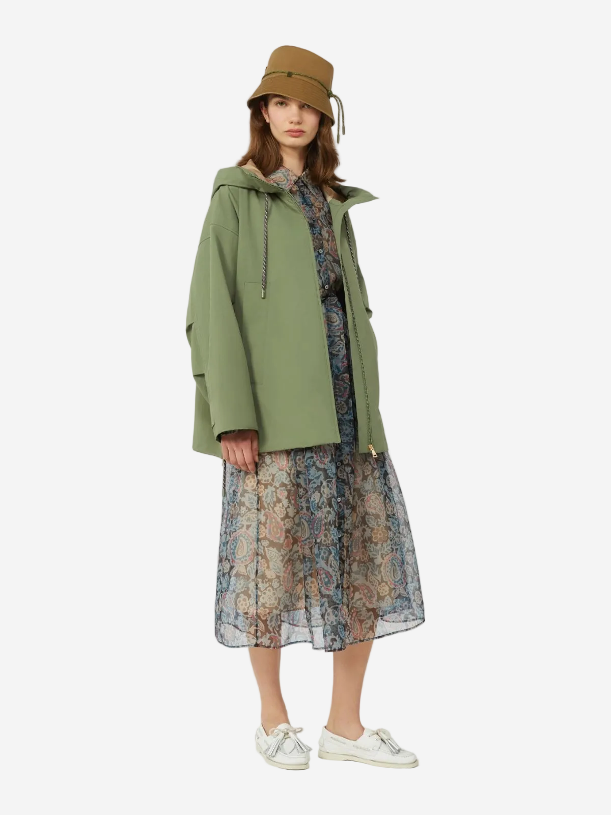 Person wearing a green coat, floral dress, and brown bucket hat on a white background