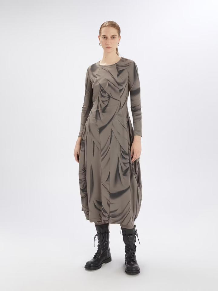 Model wearing a long, dark brown dress with a draped design on a white background