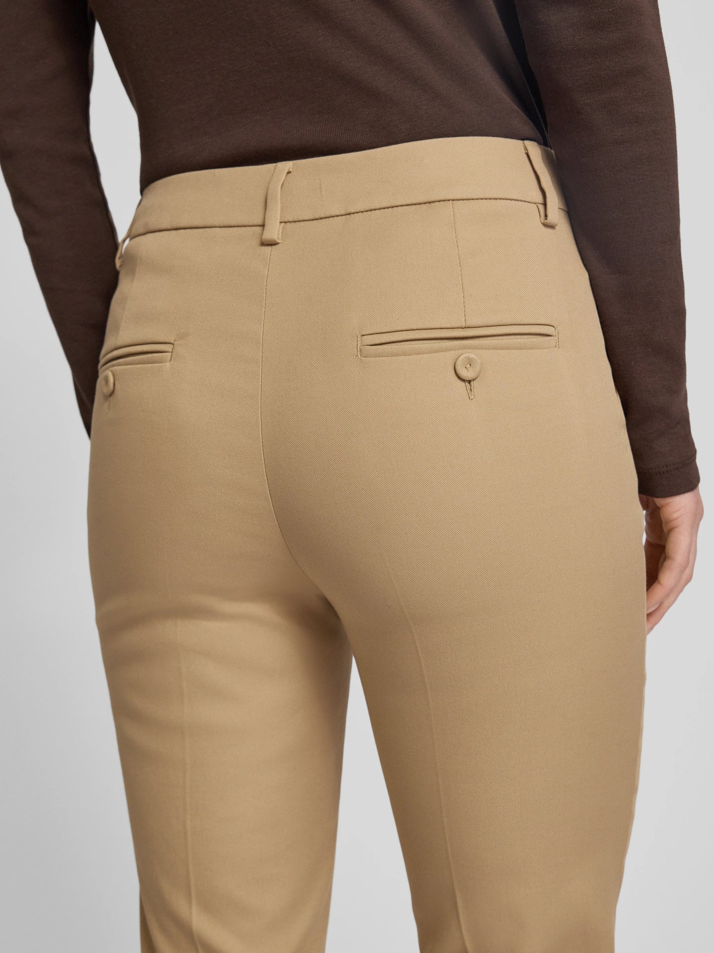 Beige pants worn by a person with a brown long-sleeve shirt on a light gray background