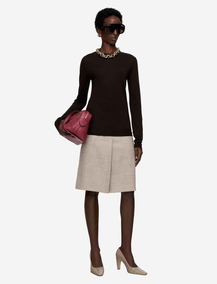Woman wearing a black long-sleeve top, beige skirt, and holding a pink handbag on a white background