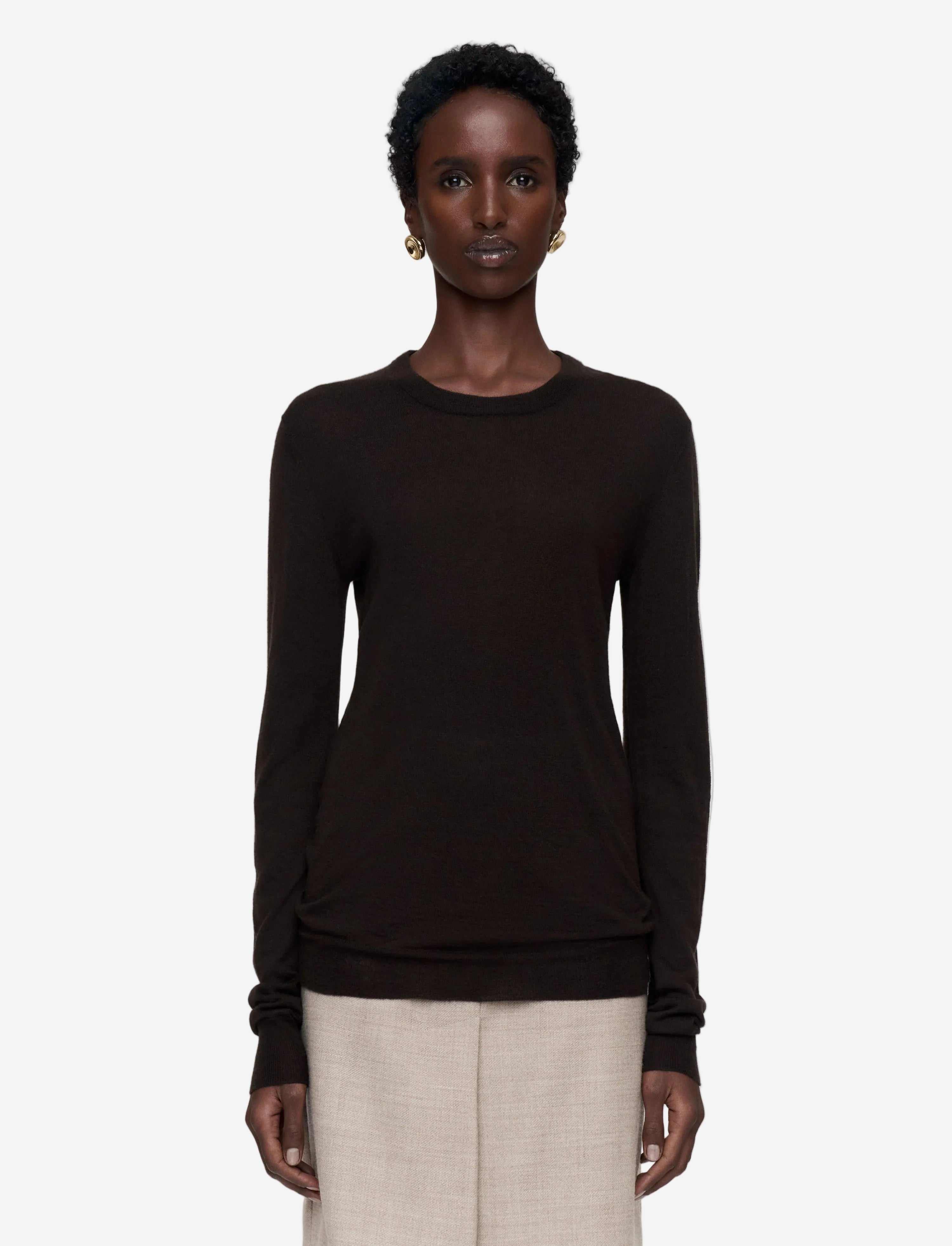 Woman wearing a black long-sleeve top and beige pants on a white background