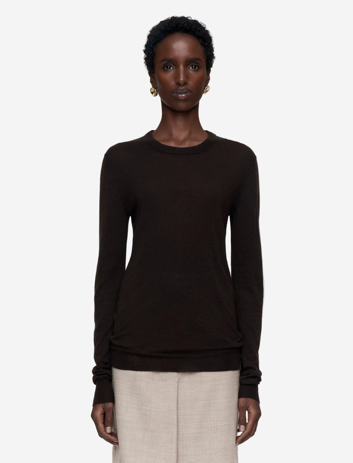 Woman wearing a black long-sleeve top and beige pants on a white background