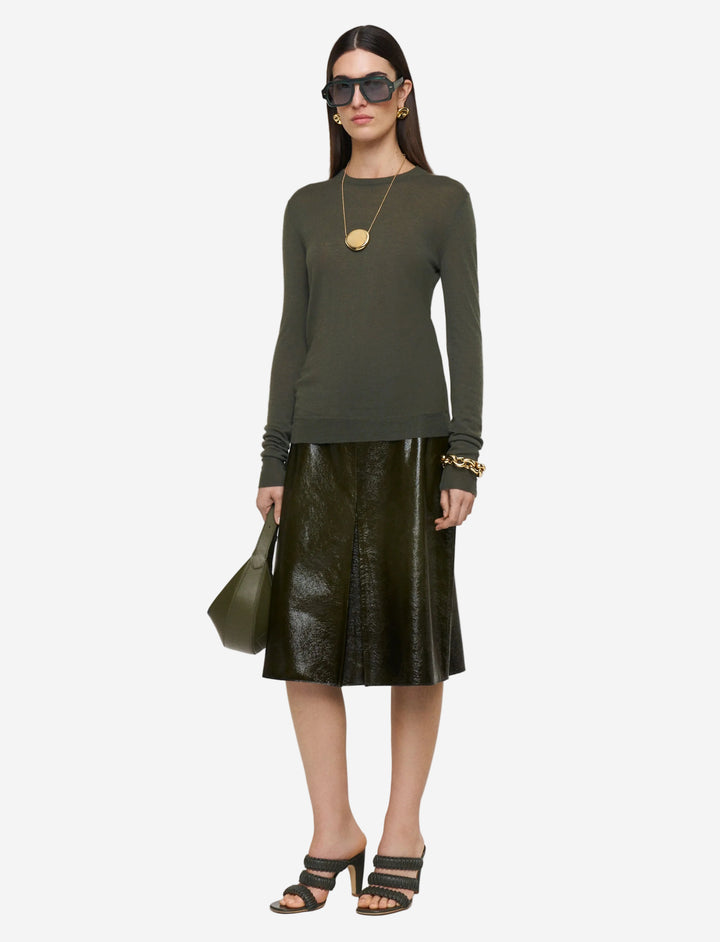 Woman wearing a green top and black leather skirt with sunglasses on a white background