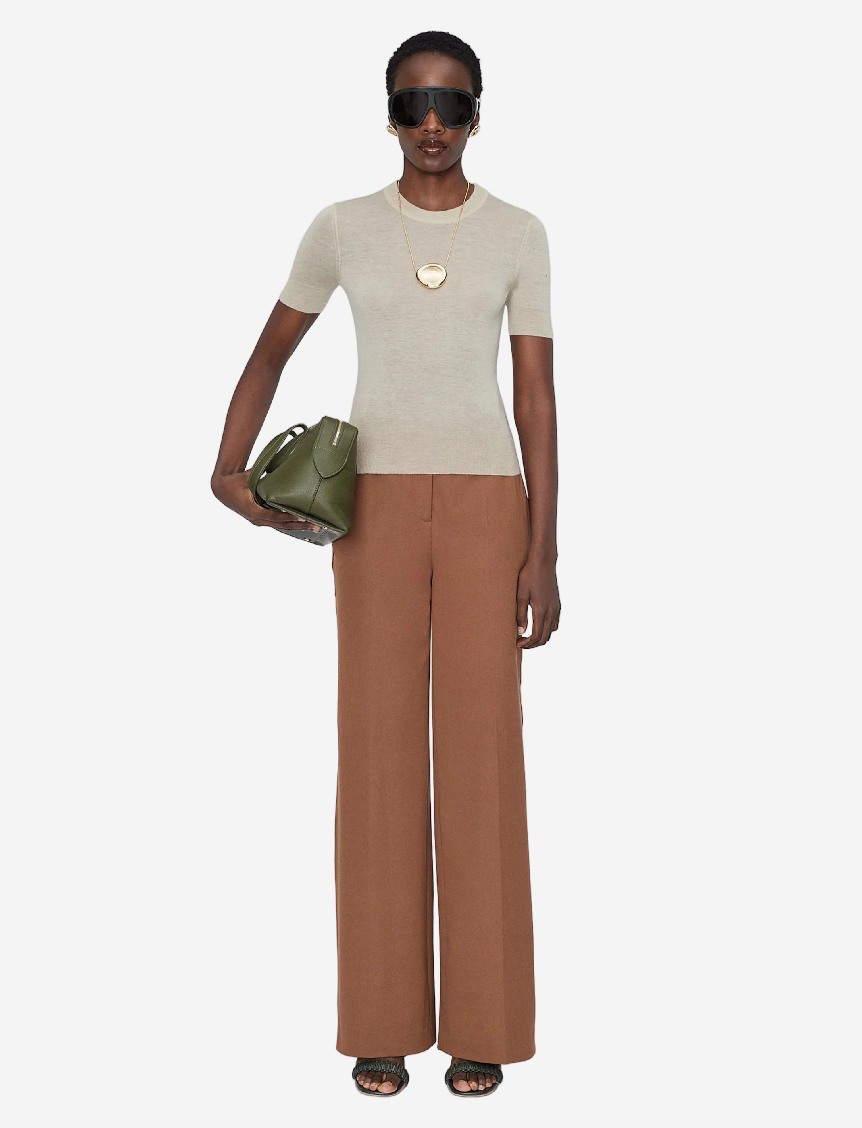 Woman wearing a beige top and brown pants, holding a green bag on a white background