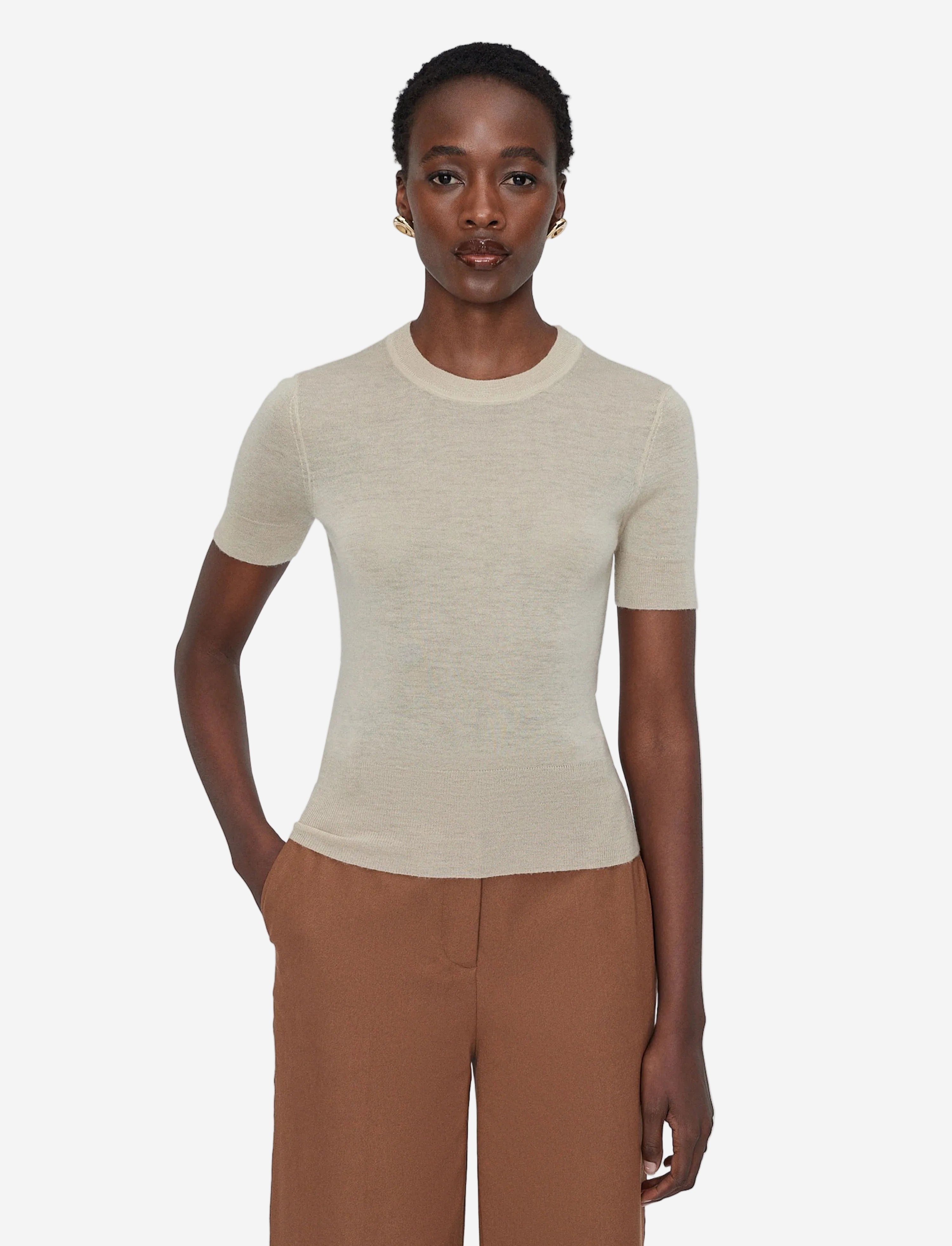 Woman wearing a beige short-sleeve sweater and brown pants on a white background